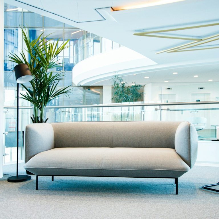 Beige Sofa mit abgerundeten Kanten in moderner Innenarchitektur, neben einer Stehlampe und Pflanzen.