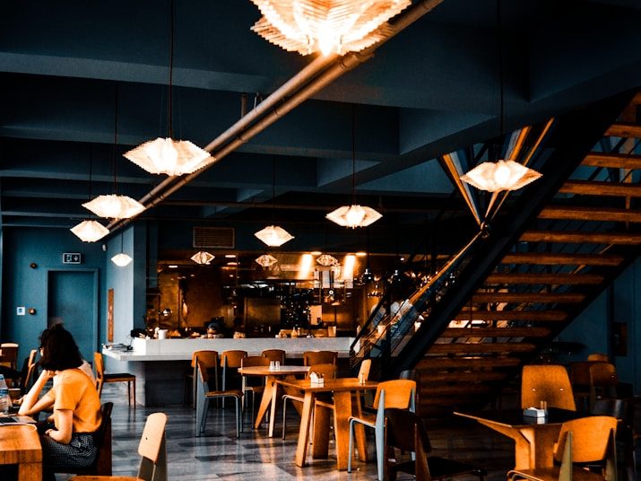 Modernes Restaurant mit Holzstühlen, offenen Treppen und stilvollen Leuchten.