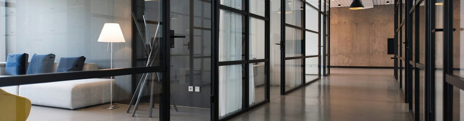 Moderne Büroumgebung mit Glaswänden, Sitzgelegenheiten und einer Stehlampe.