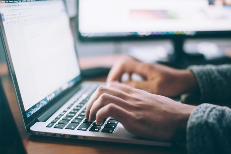Eine Person tippt auf der Tastatur eines Laptops in einem Büroumfeld.